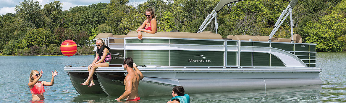 Family swimming and playing in the water around a 2020 Bennington® pontoon boat with a forest in …